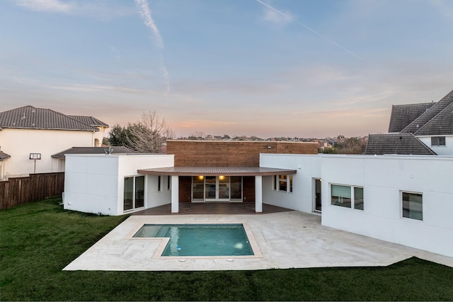 back of property at dusk featuring a yard, a patio, fence, and stucco siding