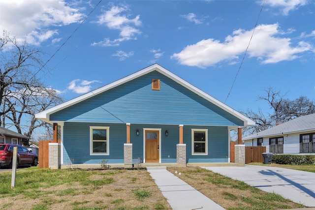 bungalow-style house featuring a front yard, covered porch, and fence