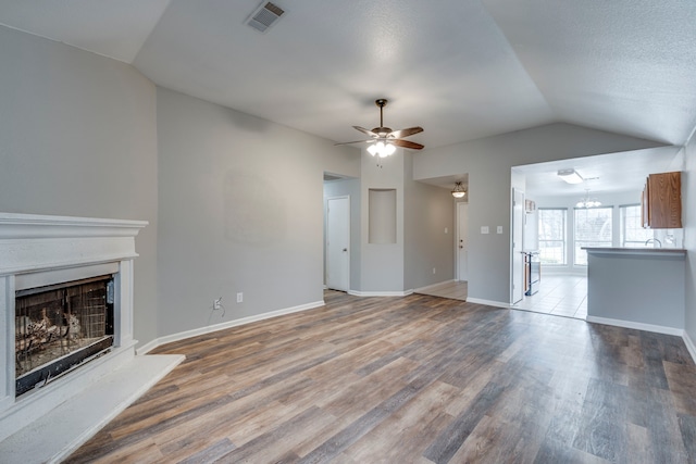 unfurnished living room featuring lofted ceiling, visible vents, a fireplace with raised hearth, wood finished floors, and baseboards