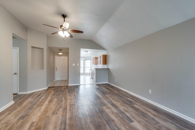 unfurnished living room featuring dark wood-style floors, ceiling fan, baseboards, and vaulted ceiling