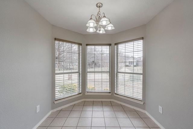 empty room featuring light tile patterned flooring, an inviting chandelier, and baseboards