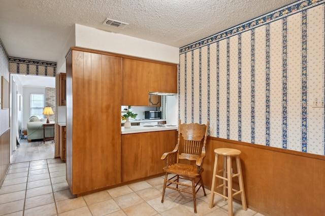 kitchen with brown cabinetry, wainscoting, stainless steel microwave, and visible vents