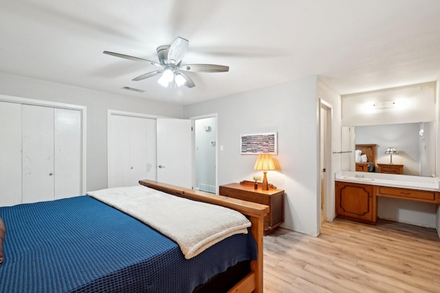 bedroom featuring two closets, visible vents, ensuite bathroom, light wood-style floors, and ceiling fan