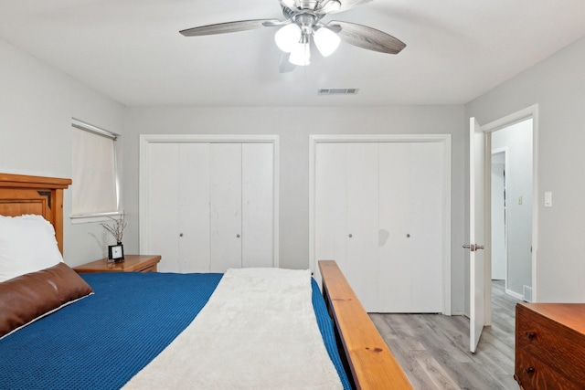 bedroom with light wood-style flooring, visible vents, ceiling fan, and multiple closets