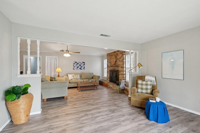 living area with a brick fireplace, visible vents, baseboards, and wood finished floors