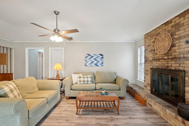 living area featuring ceiling fan, light wood-type flooring, a fireplace, and crown molding