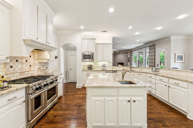 kitchen featuring stainless steel appliances, light stone counters, an island with sink, and a sink