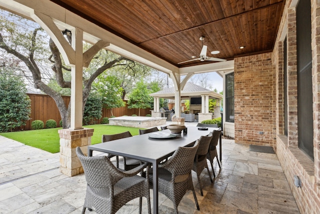 view of patio / terrace with a hot tub, a gazebo, a ceiling fan, outdoor dining space, and a fenced backyard