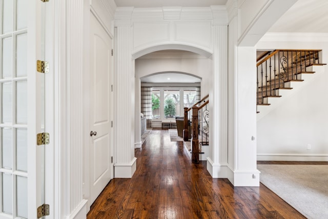 foyer featuring arched walkways, dark wood-style flooring, ornamental molding, baseboards, and stairs