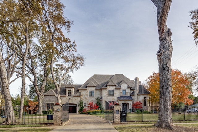 french country style house featuring a fenced front yard, decorative driveway, a chimney, a front yard, and stone siding