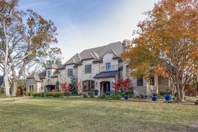 french provincial home with a chimney, metal roof, a standing seam roof, and a front yard