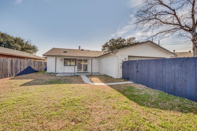 back of house with brick siding, a lawn, a patio area, a garage, and a fenced backyard