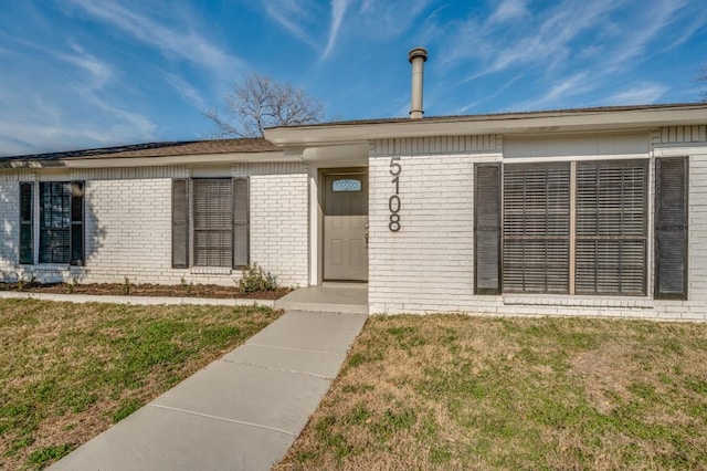 entrance to property featuring brick siding and a lawn