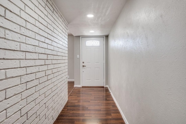 doorway to outside featuring dark wood-style floors, brick wall, and baseboards