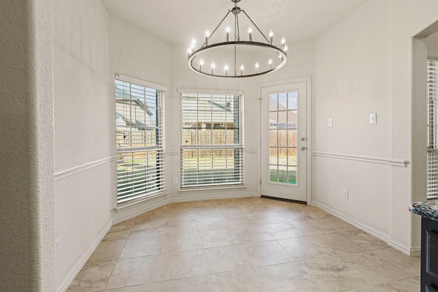 unfurnished dining area with a notable chandelier, baseboards, light tile patterned flooring, and a healthy amount of sunlight