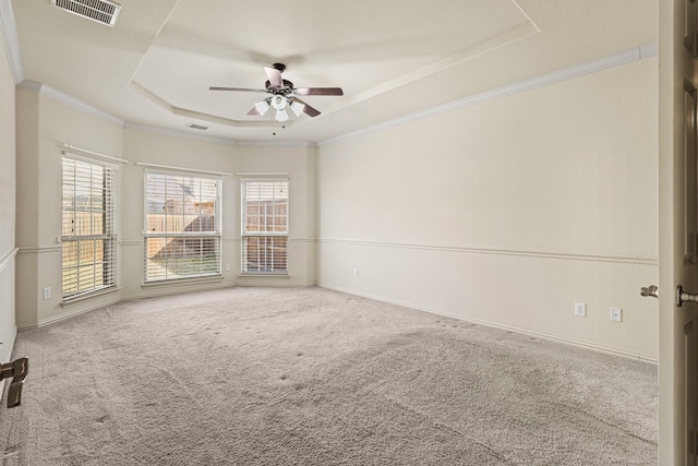 carpeted empty room featuring baseboards, visible vents, ceiling fan, a tray ceiling, and crown molding