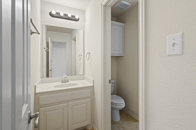 bathroom featuring a textured wall, toilet, visible vents, vanity, and baseboards