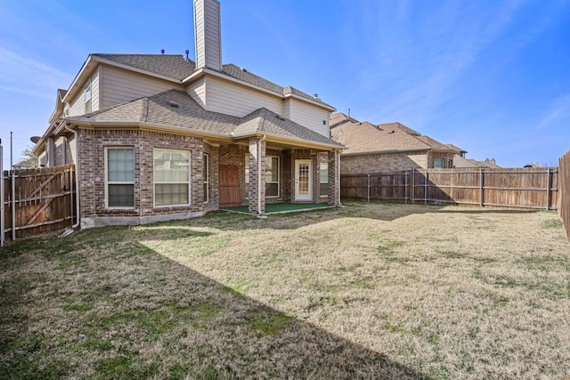 back of property with brick siding, a chimney, a shingled roof, a lawn, and a fenced backyard