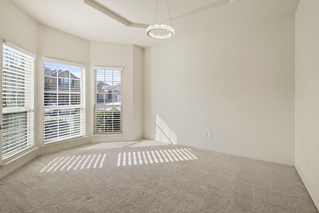 spare room featuring a tray ceiling, light carpet, and baseboards