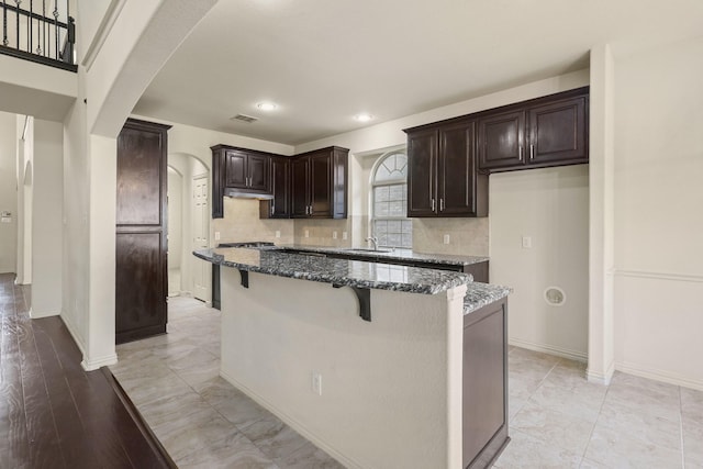 kitchen featuring visible vents, arched walkways, dark stone countertops, a center island, and under cabinet range hood