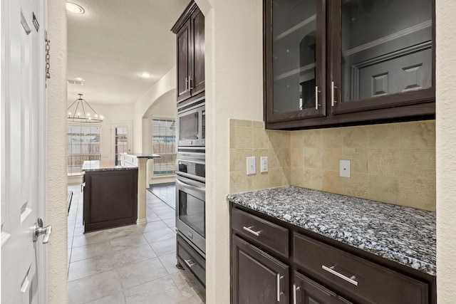 kitchen featuring stainless steel appliances, hanging light fixtures, dark stone counters, tasteful backsplash, and glass insert cabinets