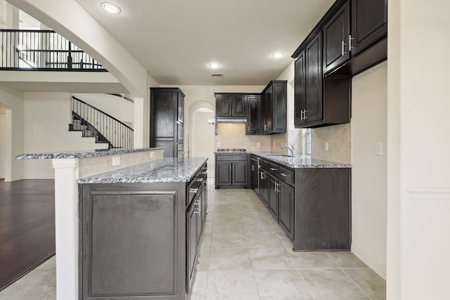 kitchen featuring light stone counters, a center island, arched walkways, decorative backsplash, and black gas stovetop