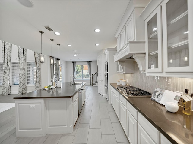 kitchen with dark countertops, visible vents, hanging light fixtures, and a kitchen island with sink