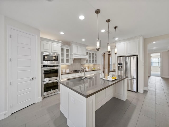 kitchen featuring arched walkways, appliances with stainless steel finishes, dark countertops, and glass insert cabinets