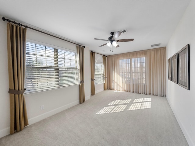 empty room with light carpet, ceiling fan, visible vents, and baseboards