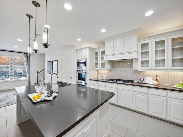 kitchen featuring a sink, white cabinetry, an island with sink, dark countertops, and glass insert cabinets