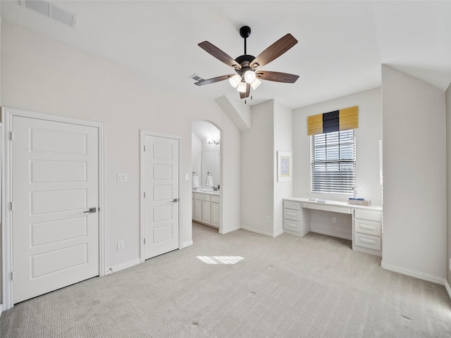 unfurnished bedroom featuring light carpet, built in desk, arched walkways, and baseboards