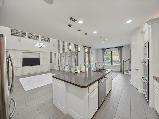 kitchen with stainless steel appliances, dark countertops, open floor plan, a kitchen island with sink, and white cabinetry