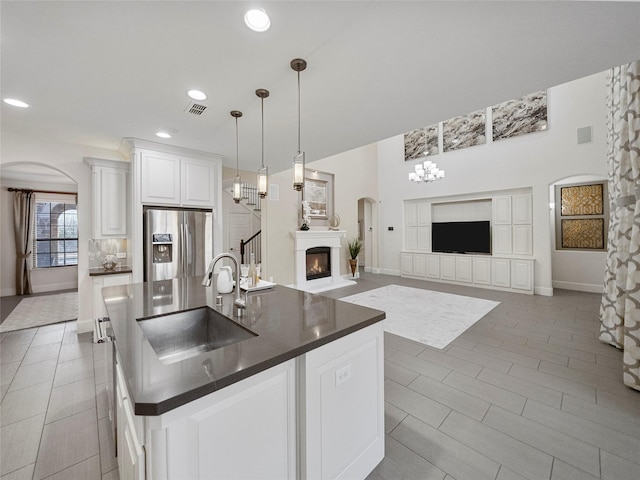 kitchen featuring stainless steel refrigerator with ice dispenser, dark countertops, a glass covered fireplace, open floor plan, and a sink