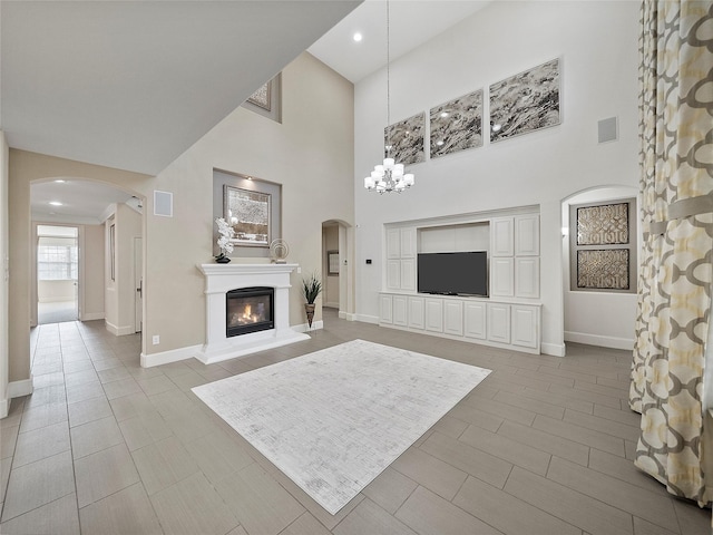 unfurnished living room featuring visible vents, arched walkways, baseboards, a glass covered fireplace, and an inviting chandelier