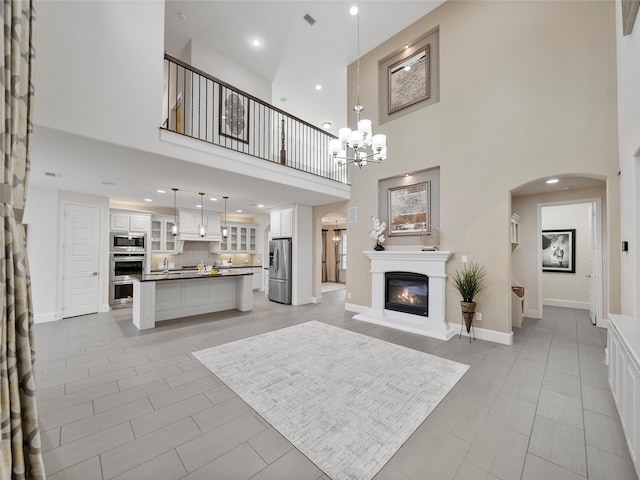 living area with visible vents, arched walkways, baseboards, a glass covered fireplace, and an inviting chandelier