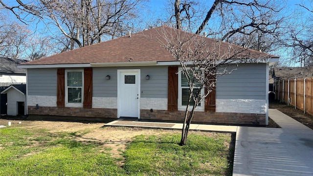 view of front of property with stone siding, roof with shingles, fence, and a front yard