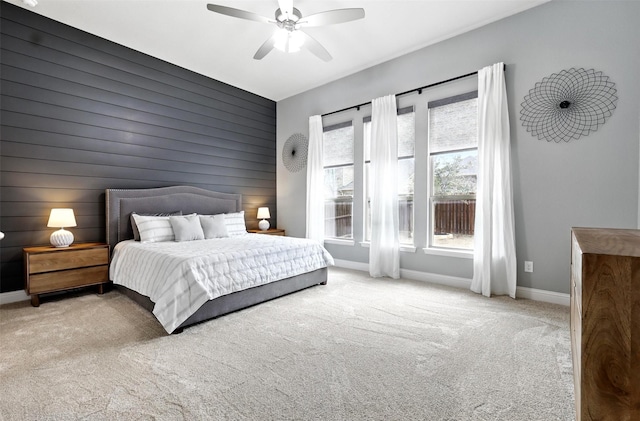 carpeted bedroom with an accent wall, wooden walls, baseboards, and ceiling fan