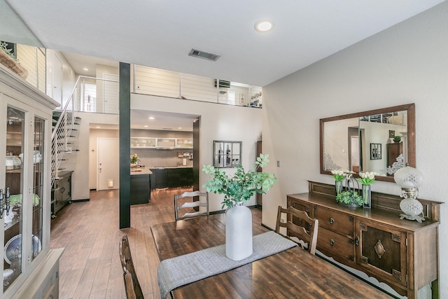 dining room featuring recessed lighting, wood finished floors, a towering ceiling, visible vents, and stairs