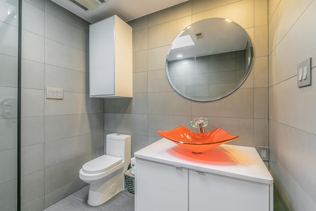 bathroom with toilet, vanity, and tile walls