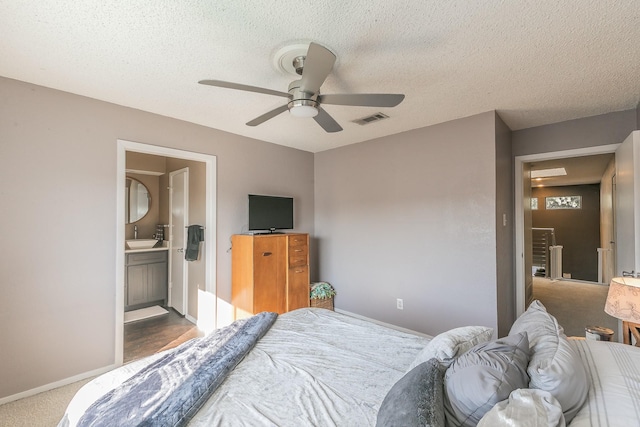 carpeted bedroom with baseboards, visible vents, a ceiling fan, ensuite bathroom, and a textured ceiling