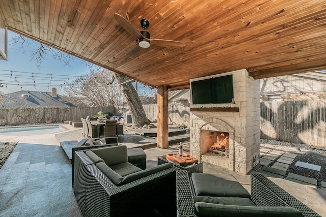 view of patio featuring an outdoor stone fireplace, a fenced backyard, a ceiling fan, and a fenced in pool