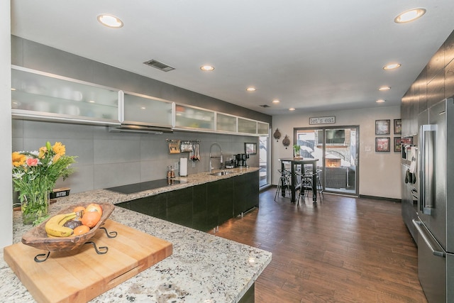 kitchen with visible vents, glass insert cabinets, light stone counters, dark wood-type flooring, and black electric stovetop