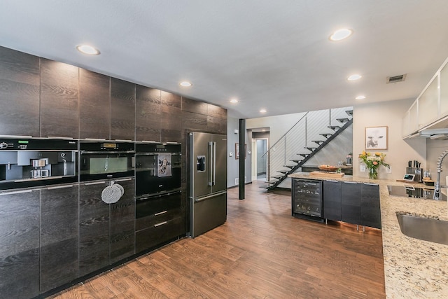 kitchen featuring light stone counters, wine cooler, wood finished floors, black appliances, and modern cabinets