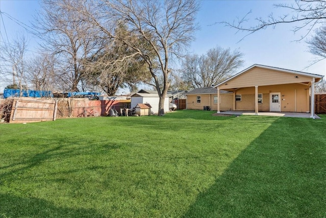 view of yard with a patio area, a fenced backyard, a shed, and an outbuilding