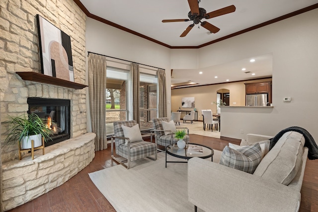 living area featuring a fireplace, wood finished floors, a ceiling fan, and crown molding