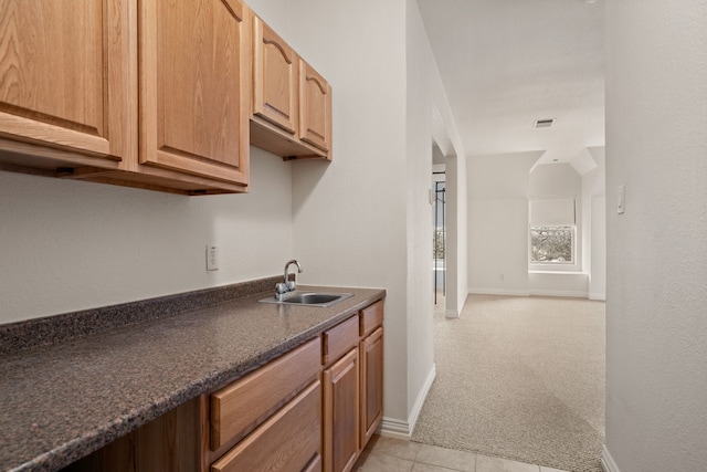 kitchen with light tile patterned floors, light colored carpet, a sink, visible vents, and baseboards