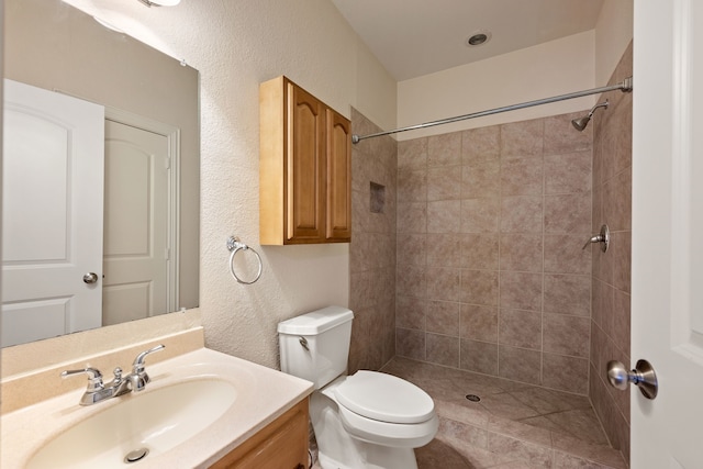 full bath featuring a textured wall, tiled shower, vanity, and toilet