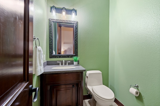 bathroom with a textured wall, vanity, and toilet