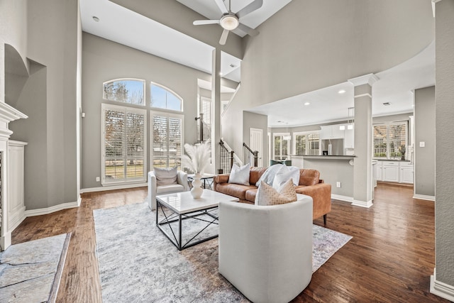 living room featuring a towering ceiling, dark wood-style floors, a fireplace, and baseboards