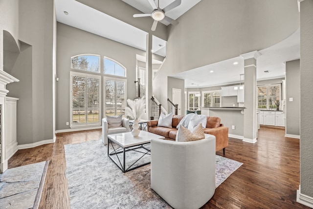 living room featuring ornate columns, dark wood-style flooring, a fireplace, and baseboards